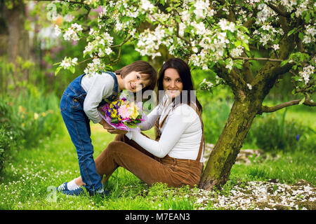 Young pregnant woman, receiving bouquet of colorful flowers from her child for Mothers Day, sitting in a beautiful spring blooming garden Stock Photo