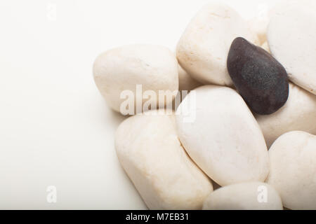 Water washed smooth white pebbles with a single black one on a white background with copy space in a conceptual image Stock Photo
