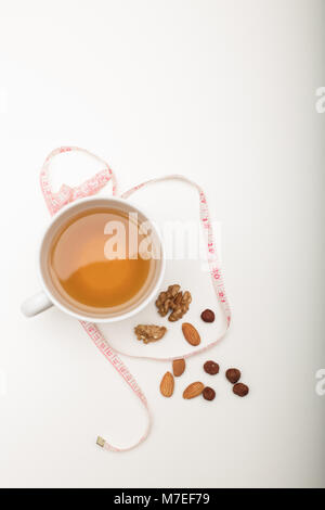 Cup of tea with assorted dried nuts and tape measure viewed from above in a healthy diet and weight loss concept on white Stock Photo