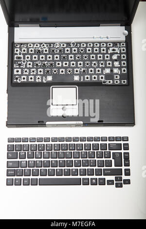 Open laptop with the alphanumeric key coverings from the keyboard removed and placed in order on a white surface in front of the computer viewed from  Stock Photo