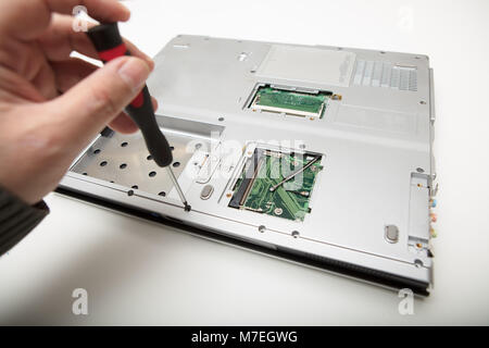 Man doing adjustments and repairs to his laptop computer using a precision screwdriver in a close up view of his hands and the disassembled laptop on  Stock Photo