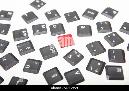 Conceptual image of individuality with loose grey key covers from a laptop keyboard with single unique red key in the center over white Stock Photo