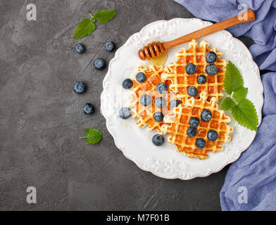 Viennese waffles with honey and fresh berries blueberry and mint on black surface. Delicious dessert. Copy space Stock Photo
