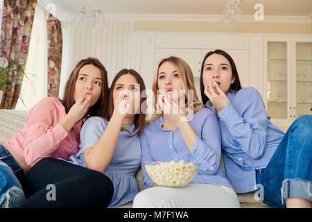 Young girls watching TV, eating popcorn sitting on the couch. Stock Photo