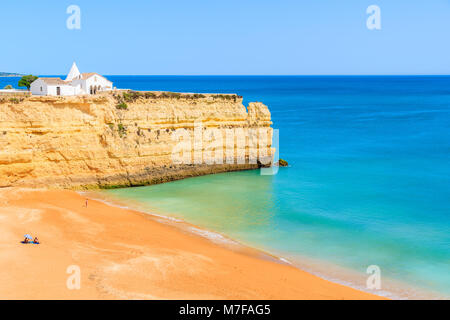 View of beach with rock cliffs and white church in Armacao de Pera town, Algarve, Portugal Stock Photo