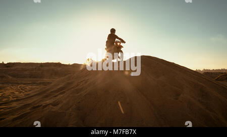 Professional Motocross Rider on FMX Motorcycle Drives on the Sand Dune and Stops There to Admire Scenic Sunsetting View. Stock Photo