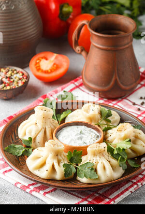 Khinkali - Georgian dumplings with meat and parsley in a ceramic dish with a sauce of sour cream and greens. Selective focus Stock Photo