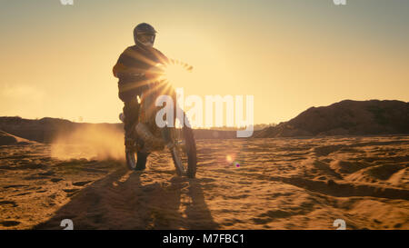 Low Angle Shot of the Professional Motocross Motorcycle Rider Standing on the Path of the Off-Road Track. It's Sunset and Track is Covered with Smoke Stock Photo