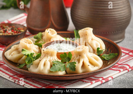 Khinkali - Georgian dumplings with meat and parsley in a ceramic dish with a sauce of sour cream and greens. Selective focus Stock Photo