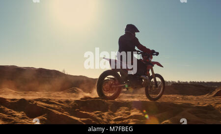 Side View Footage of the Professional Motocross Motorcycle Rider Driving on the Dune and Further Down the Off-Road Track. It's Sunset. Stock Photo