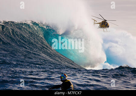 A helicopter filming a tow-in surfer at Peahi (Jaws) off Maui. Hawaii.  The head in the foreground is driving a jetski. Stock Photo