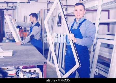 Smiling production workers in coverall with different PVC windows and doors Stock Photo