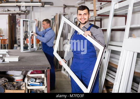 Production smiling spanish workers in coverall with different    finished PVC profiles and windows at factory Stock Photo