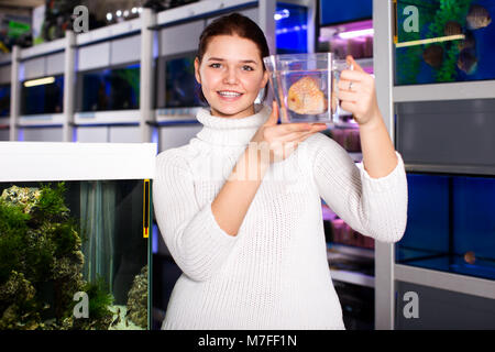 Happy teenager keeps big tropical fish in plastic container with water in aquarium fish shop Stock Photo