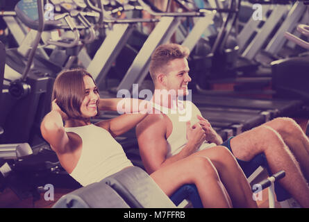 Well trained attractive young man and woman training abdominal muscles doing sit ups in gym Stock Photo