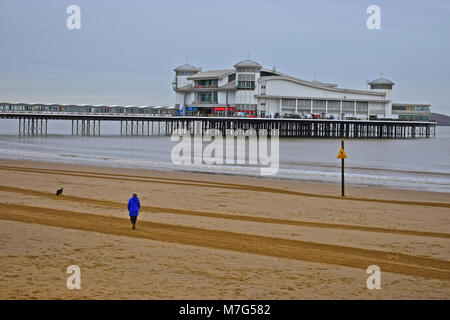 A lone lady walking her dog along the beach by The Grand Pier at Weston-super-Mare in Winter Stock Photo