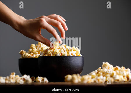 The hand reaches for a bowl with tasty popcorn. Still-life on a wooden background. Stock Photo