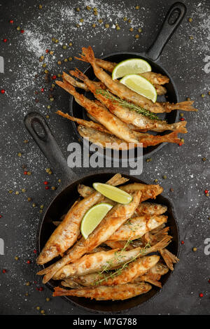 Fried smelt in a frying pan on the table with spices, lime and thyme. Small crispy fish. Selective focus Stock Photo