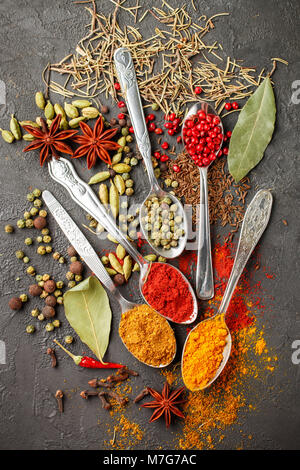 Variety of natural spices, seasonings and herbs in spoons on the stone table - paprika, coriander, cardamom, turmeric, rosemary, salt, pepper, cumin,  Stock Photo