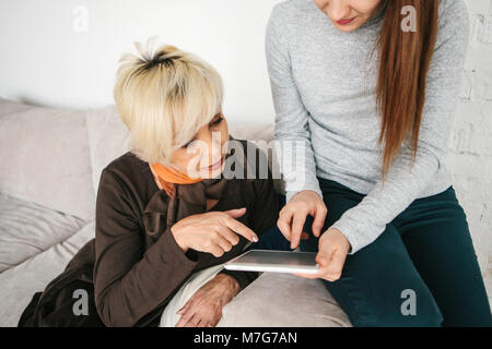 A young girl explains to an elderly woman how to use a tablet or shows some application or teaches you how to use a social network. Teaching the older generation of new technologies. Stock Photo