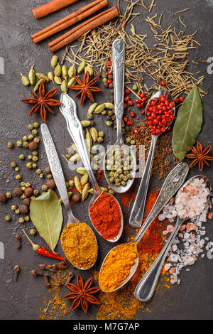 Variety of natural spices, seasonings and herbs in spoons on the stone table - paprika, coriander, cardamom, turmeric, rosemary, salt, pepper, cumin,  Stock Photo