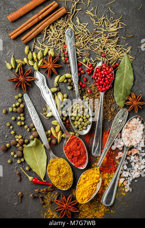 Variety of natural spices, seasonings and herbs in spoons on the stone table - paprika, curry, coriander, cardamom, turmeric, rosemary, salt, pepper,  Stock Photo