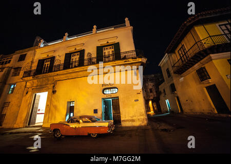 A classic American car parked outside a pharmacy in Havana, Cuba, at night Stock Photo