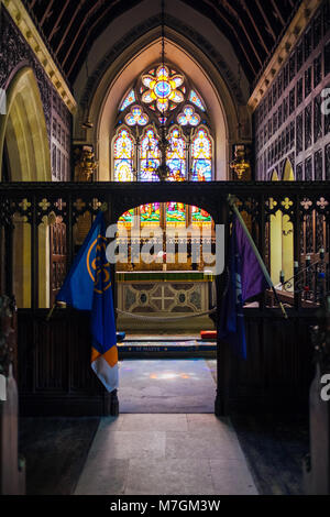 The beautiful stained glass window in St. Mary’s church flanked by scout and guide flags, Brownsea Island, Poole, Dorset, UK Stock Photo