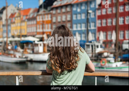 Tourist woman admiring the city, sitting at the Nyhavn harbor pier Copenhagen, Denmark. Visiting Scandinavia. Stock Photo