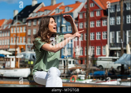 Tourist woman admiring the city, sitting at the Nyhavn harbor pier Copenhagen, Denmark. Visiting Scandinavia. Stock Photo