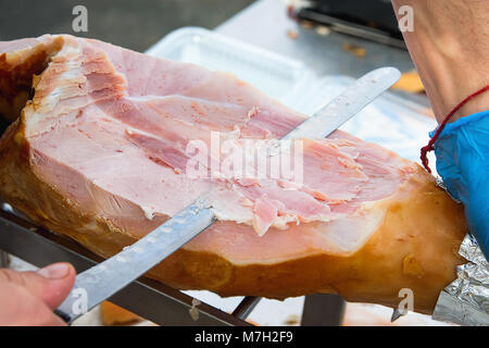 Farmer Slicing with Long Knife Smoked Baked Pork Ham from Leg at Market. Close up of Meat Texture. Vibrant Colors. Organic Produce. Travel Lifestyle.  Stock Photo