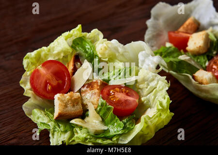 Yummy top view composition of fresh healthy salad artistically served on lettuce leaves on vintage wooden table. Traditional Caesar salad with lettuce Stock Photo