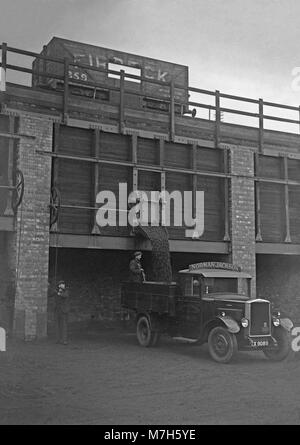 Coal being loaded onto a delivery truck via a vertical coal drop, (staithe or shute) directly from a railway wagon above it c. 1950. These were a common sight at railway sidings when coal was used as the main form of domestic heating after World War II - this one was located near Leeds, West Yorkshire, England, UK Stock Photo