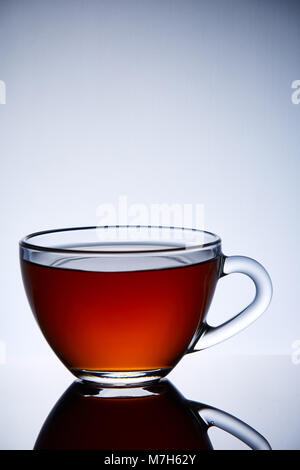 Glass transparent empty teacup on a light grey background, reflected in the surface, close-up. Helium filter gives a beautiful unusual futuristic ligh Stock Photo