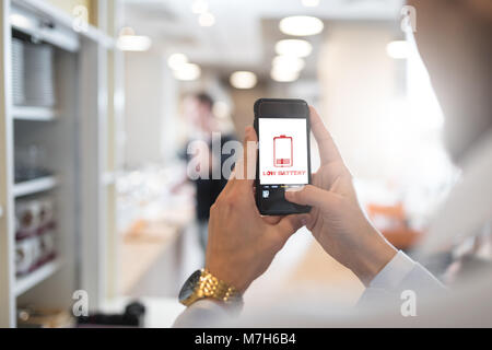 Businessman holding mobile phone with low battery symbol and battery Stock Photo