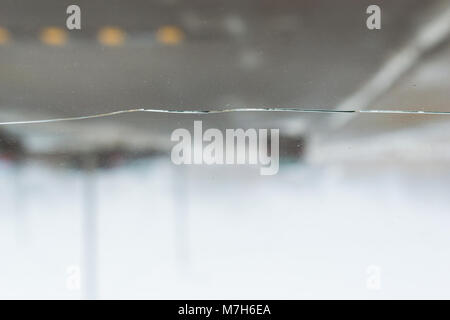 Broken car glass with crack on windshield of auto. Blurred grey backdrop of transport road in background Stock Photo