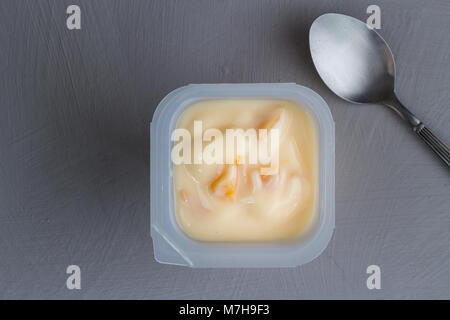 Healthy peach fruit flavored yoghurt with natural coloring in plastic cup isolated on gray texture background with small silver spoon - top view Stock Photo