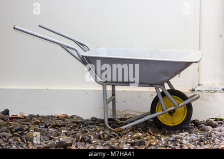 yellow wheelbarrow on wet river stones Stock Photo