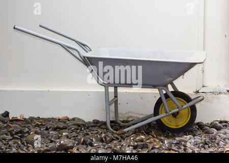 yellow wheelbarrow on wet river stones Stock Photo