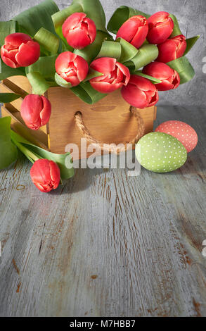 Spring celebration background: bunch of red tulips, spring decorations and painted eggs on gray rustic background, text space Stock Photo