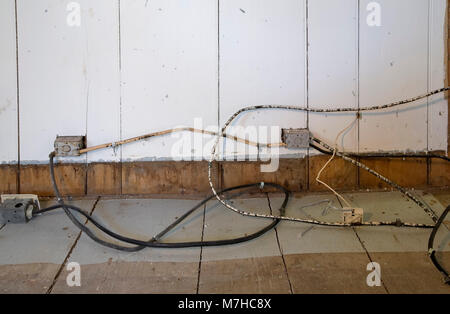 Old electrical cloth insulated wiring and outlets on wooden floor and wall in empty inside an old 1800s cottage style home. Stock Photo