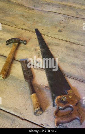Old hammer, wood chisel and saw on wooden floor in empty room inside an old 1800s cottage style home. Stock Photo