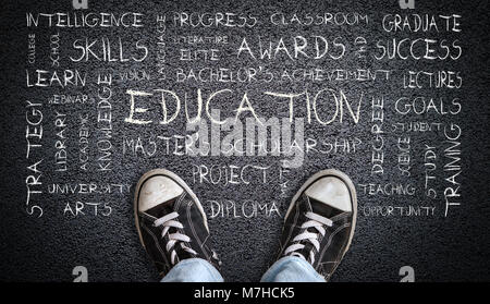 A teenager in jeans and canvas shoes standing on asphalt road with Education word cloud. Concept of stepping into education and its significance. Stock Photo