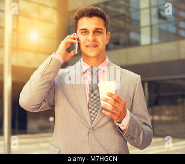 Business man talking on mobile phone outdoors with disposable cup in hand Stock Photo