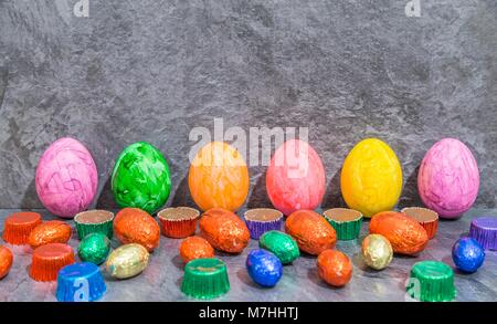 Colorful Easter eggs with chocolate easter eggs and sweet meat in front of grey background Stock Photo