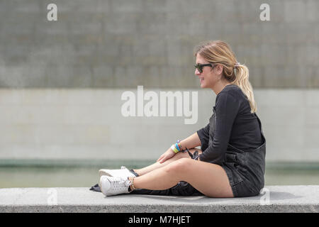 Young blonde lady with Ponytail, sitting on wall relaxing, Bilbao, Vizcaya, Pais Vasco, Spain, Stock Photo