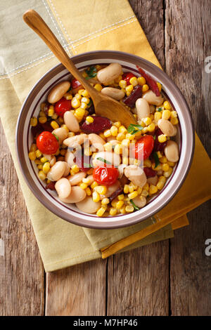 succotash of corn, butter beans, tomatoes and bacon close up in a bowl on the table. Vertical top view from above Stock Photo