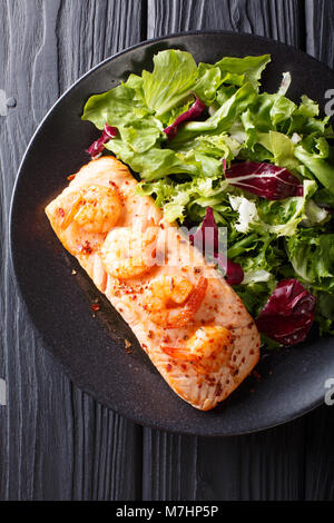 Delicious food: baked salmon with prawns in honey sauce and fresh salad on a plate close-up on a table. Vertical top view from above Stock Photo