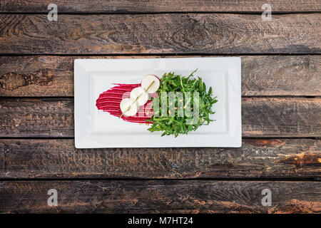 Salad - bakes beetroot slices, goat cheese, fresh arugula and pine nuts, served on the white plate. Stock Photo