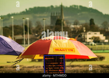 Hereford, Herefordshire, UK. 10th March, 2018. A book makers umbrella is seen in front of Hereford Cathedral and a church spire at Hereford racecourse during Ladies Day in Hereford on 10th March 2018. Credit: Jim Wood/Alamy Live News Stock Photo